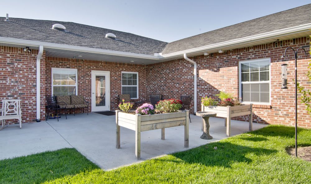 A sunny patio area with planters, set against a brick house and well-kept lawn.