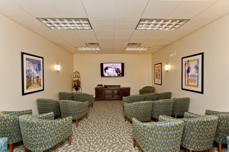 A well-lit waiting room with patterned chairs facing a television.