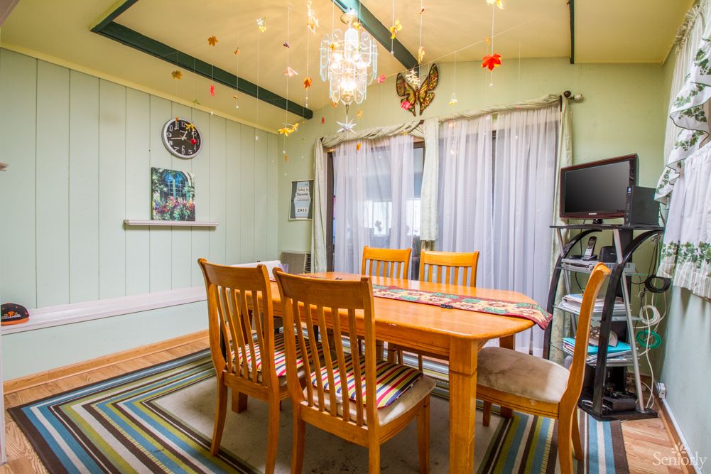 A cozy dining room featuring a wooden table with chairs, illuminated by a chandelier and adorned with colorful ceiling decorations and striped rug.