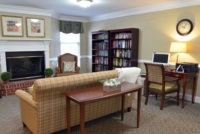 A cozy living room with a sofa, armchair, fireplace, bookshelf, and computer desk.