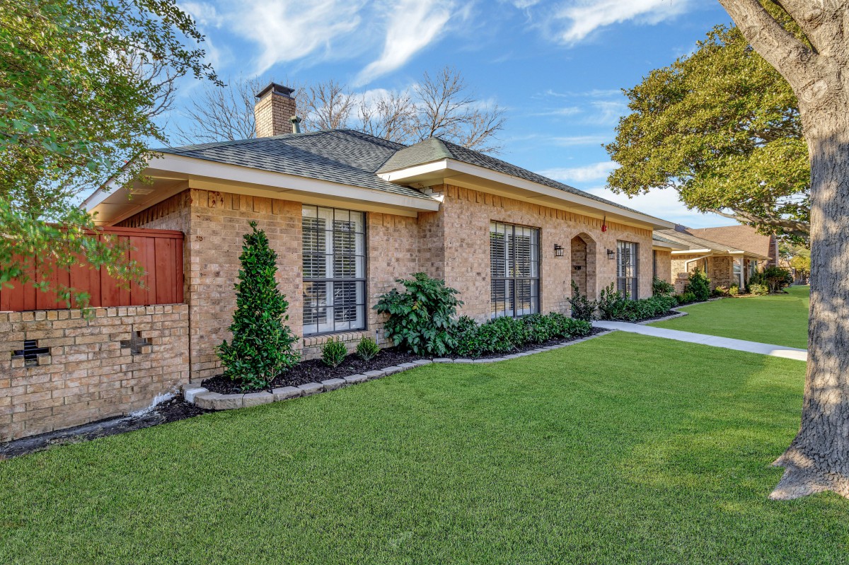 A single-story brick house with well-maintained landscaping and a lush green lawn.