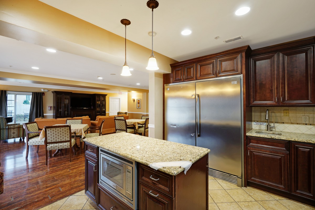 Modern kitchen with granite island and stainless steel refrigerator, leading to a spacious dining area.