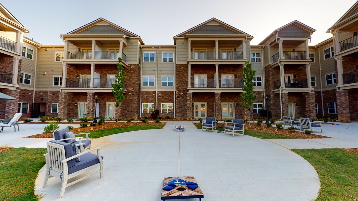 A modern apartment complex with a spacious outdoor area featuring lawn chairs and a cornhole game setup.