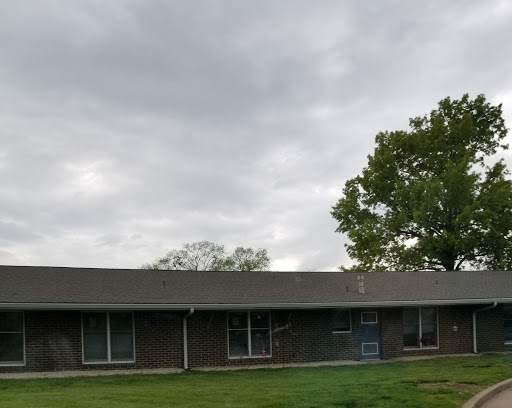 A modest building surrounded by grassy areas and trees under a cloudy sky.
