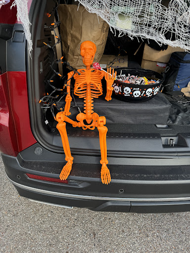 An orange skeleton sits casually in the trunk of a car, ready for Halloween fun.