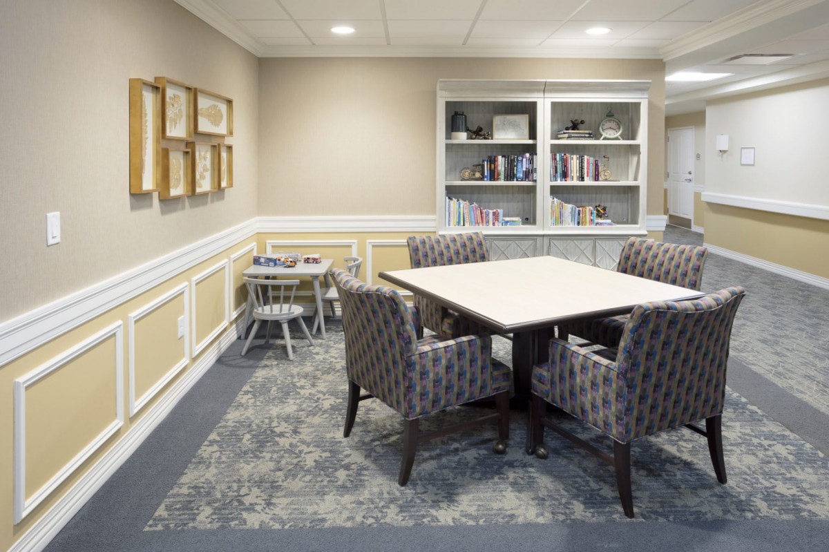 A cozy room with a table, patterned chairs, bookshelves, and framed artworks on the wall.