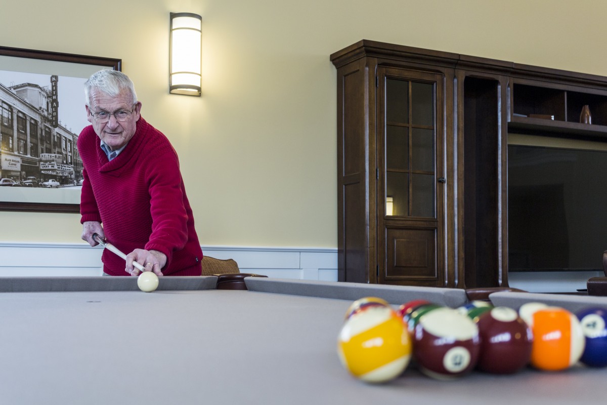 A man in a red sweater lines up a shot on a pool table indoors.