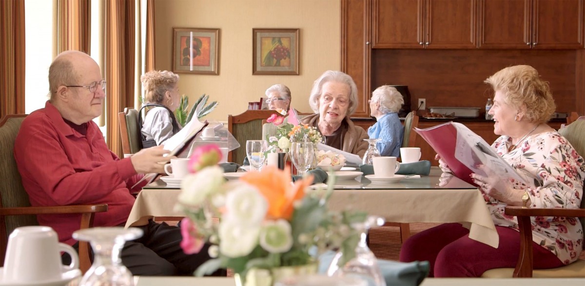 A group of elderly people enjoying a meal together at a beautifully set table with flowers.