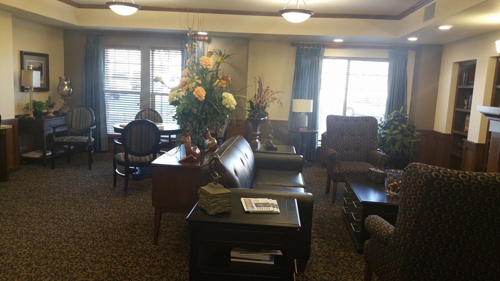 A cozy living room with sofas, chairs, and floral decorations near large windows.