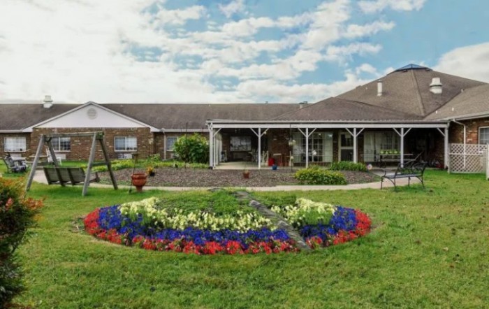 A beautifully maintained garden with colorful flowerbeds in front of a house under a partly cloudy sky.