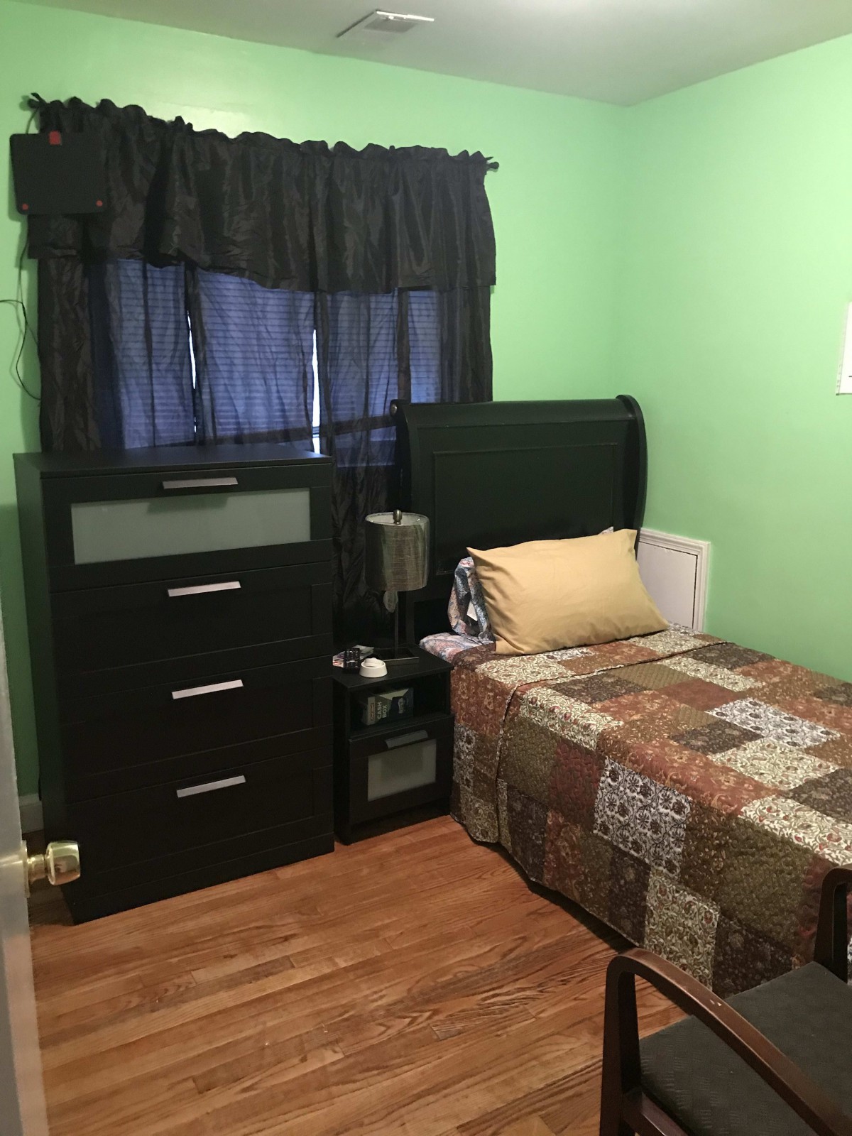 A cozy bedroom with green walls, featuring a single bed and a dresser.