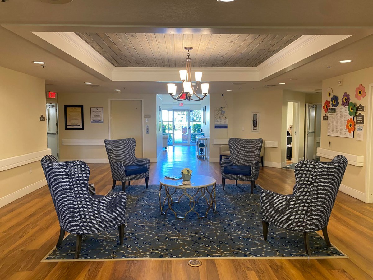 A cozy lobby with a seating area featuring armchairs around a central table, accented by a chandelier and a patterned rug.