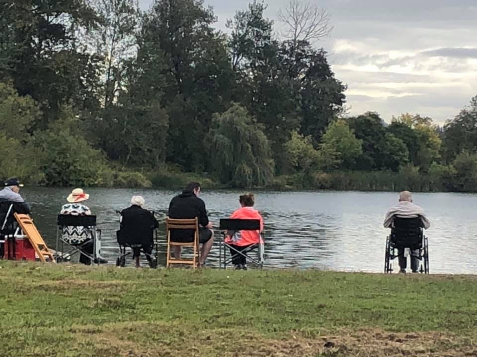 A group of people sitting on chairs by the lake, enjoying the serene outdoor setting.