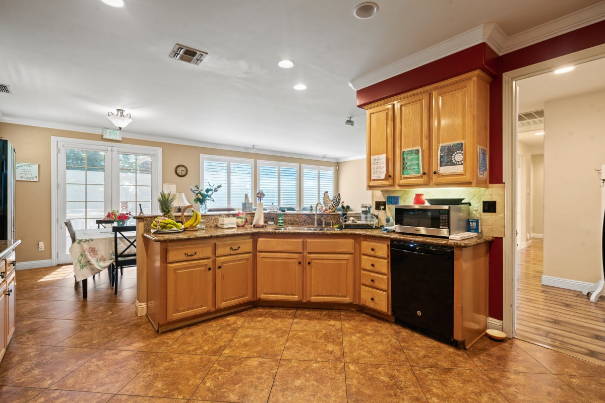 A spacious and modern kitchen with wooden cabinets, featuring a black dishwasher and various appliances on the countertop.