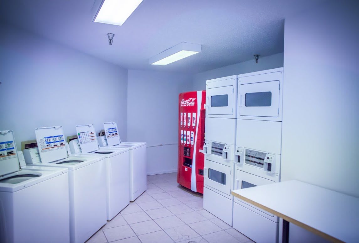 A self-service laundry room featuring washing machines, dryers, and a vending machine.