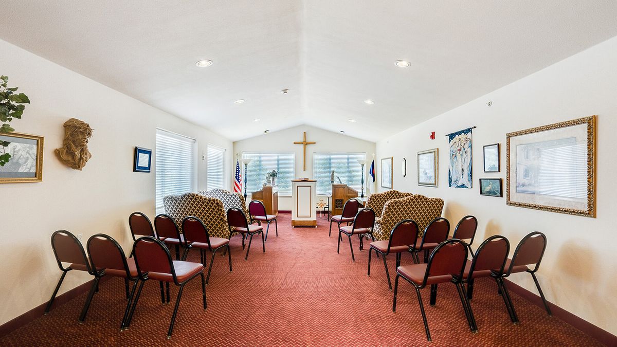 A small chapel interior with rows of chairs, a pulpit, and a cross on the wall.