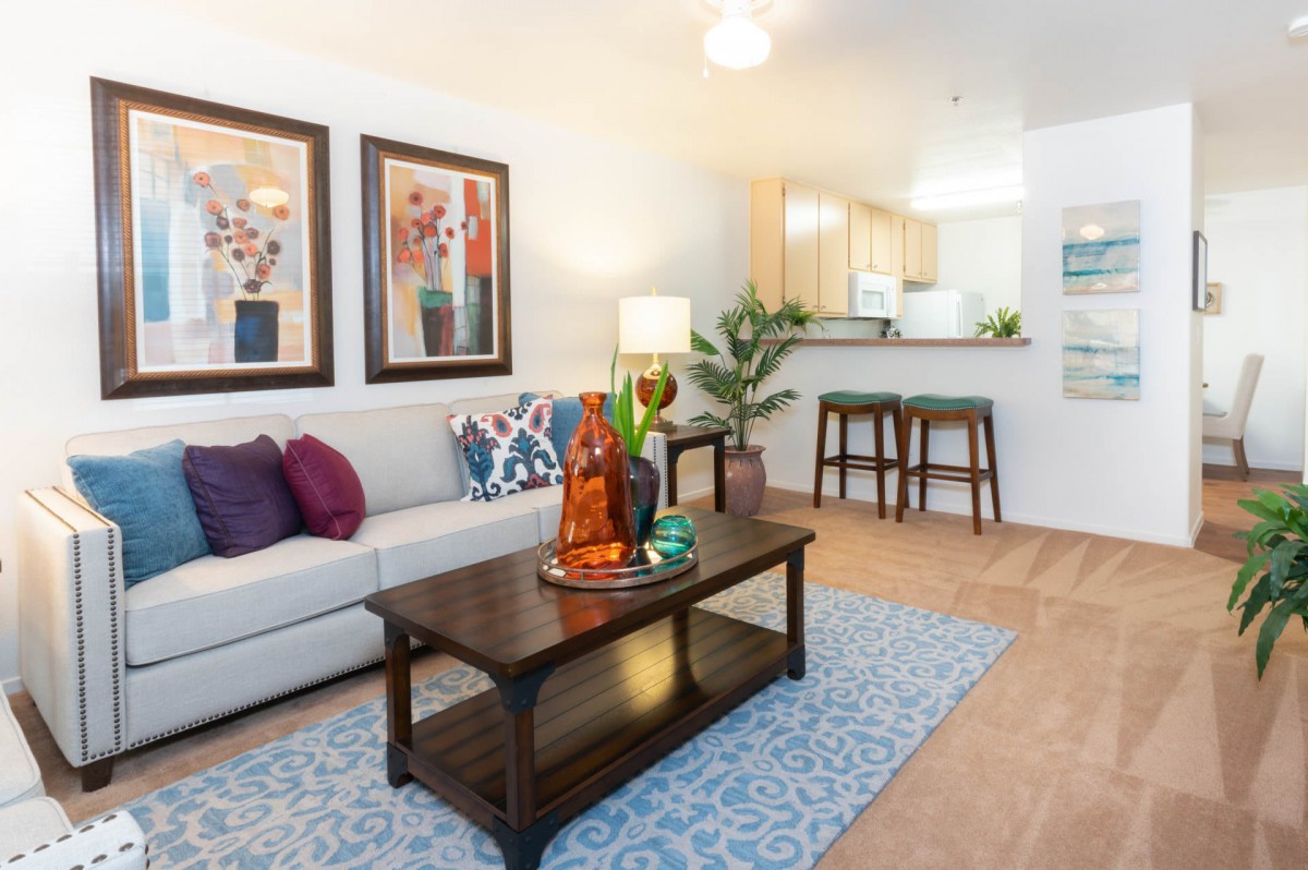 A modern living room with a comfortable sofa, colorful artwork, and a stylish coffee table near the kitchen area.