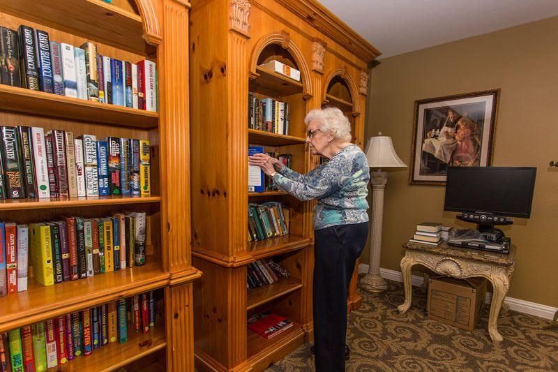 A woman is selecting a book from a wooden bookshelf in a cozy home library.