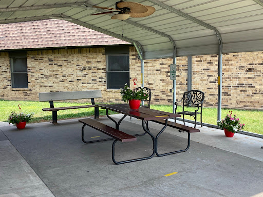 A cozy outdoor patio area featuring a table, chairs, and decorative flowers under a sheltered roof.