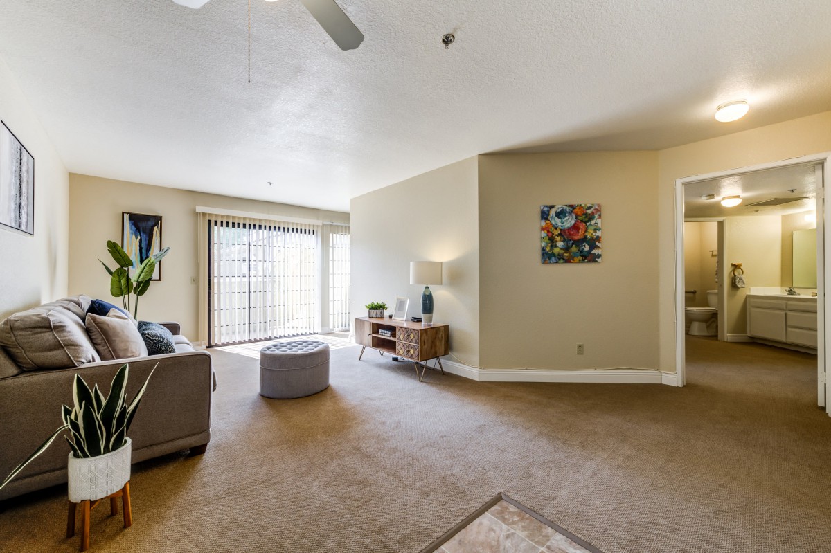 A spacious living room with a sofa, ottoman, and large windows letting in natural light.