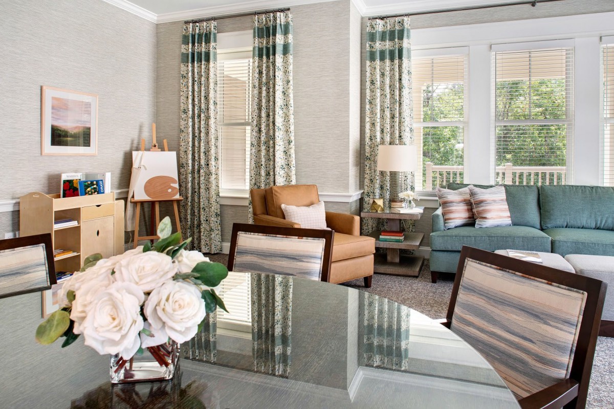 A beautifully decorated living room featuring comfortable seating, elegant curtains, and a glass-top table adorned with flowers.