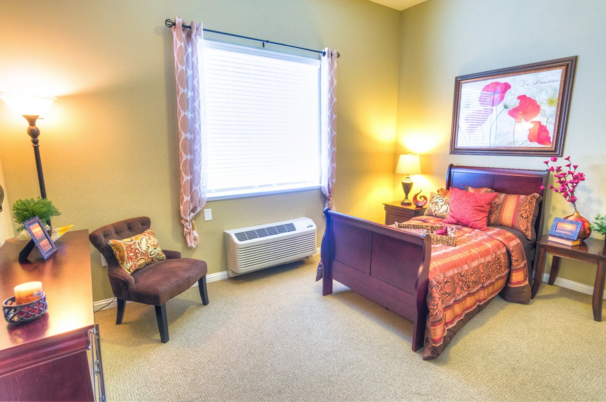 A cozy bedroom with a bed, chair, and lamp by the window.