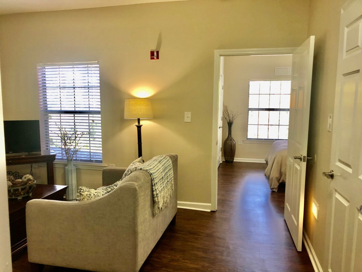 Cozy living room with sofa and lamp leading to a bedroom.