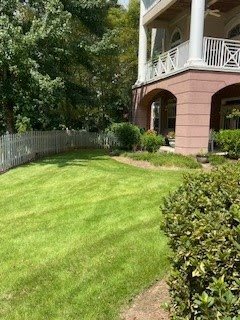 A well-maintained lawn beside a residential building with a white fence.