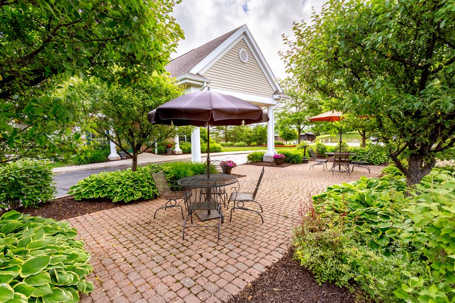 A peaceful garden patio with outdoor seating and umbrellas, surrounded by lush greenery.