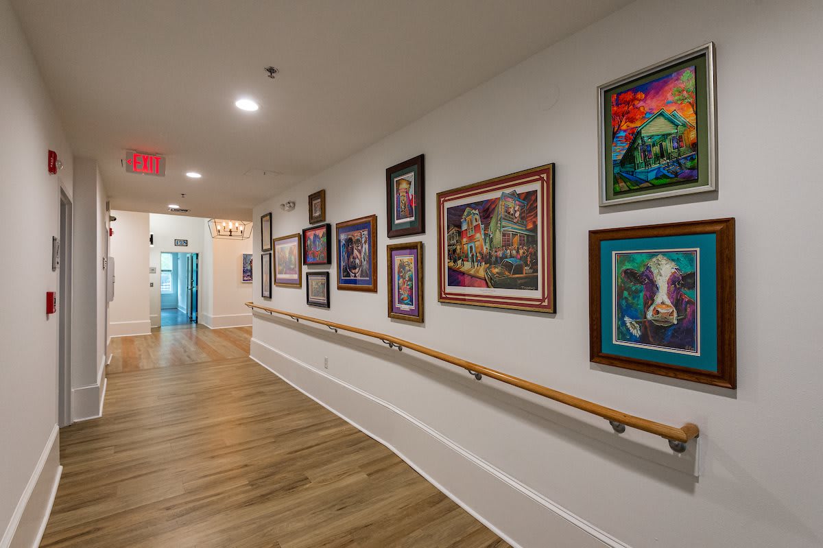 A hallway decorated with a variety of framed paintings on the wall, featuring a wooden floor and soft lighting.