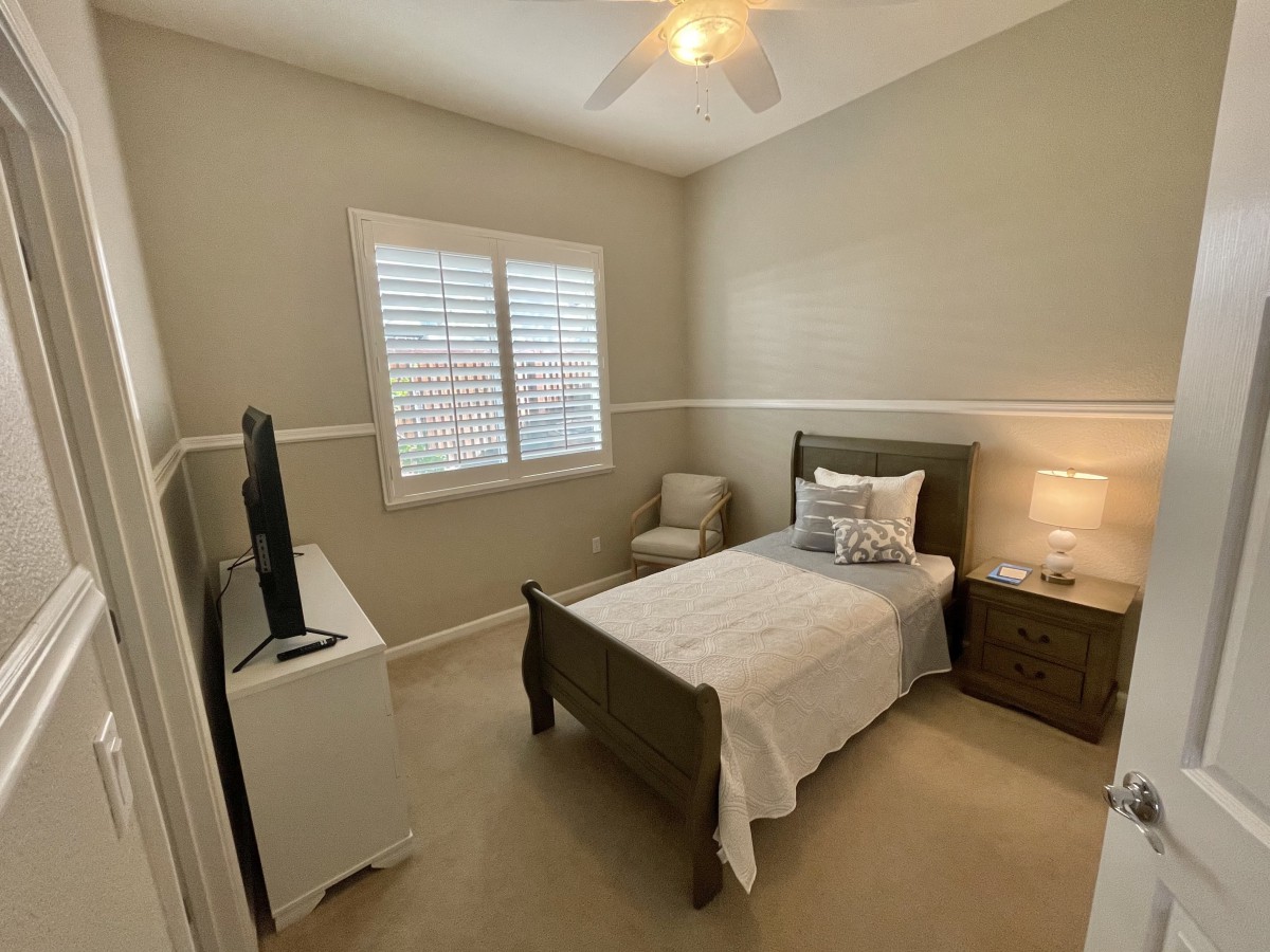 A cozy bedroom featuring a single bed, nightstand with a lamp, and a TV stand opposite the bed.