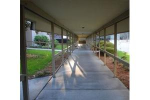 A covered outdoor walkway with railings, leading through a grassy area.