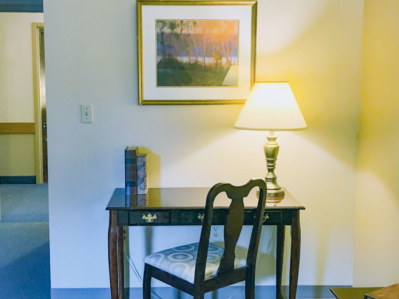 A cozy study nook with a wooden desk, chair, and lamp, complemented by a painting on the wall.