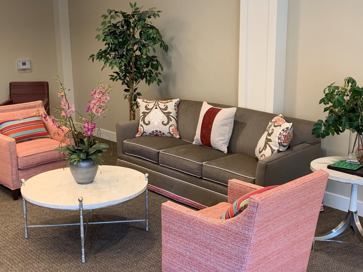 A cozy living room setting featuring a gray sofa, pink chairs, and a white coffee table adorned with a plant.