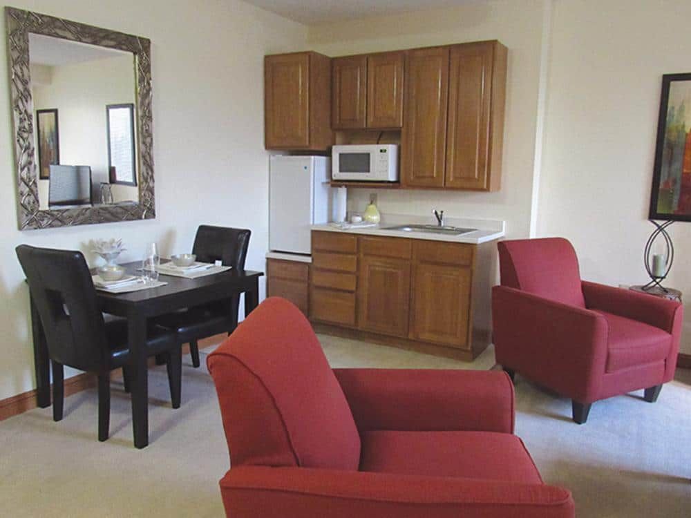 A cozy apartment living area with a kitchenette and red armchairs.