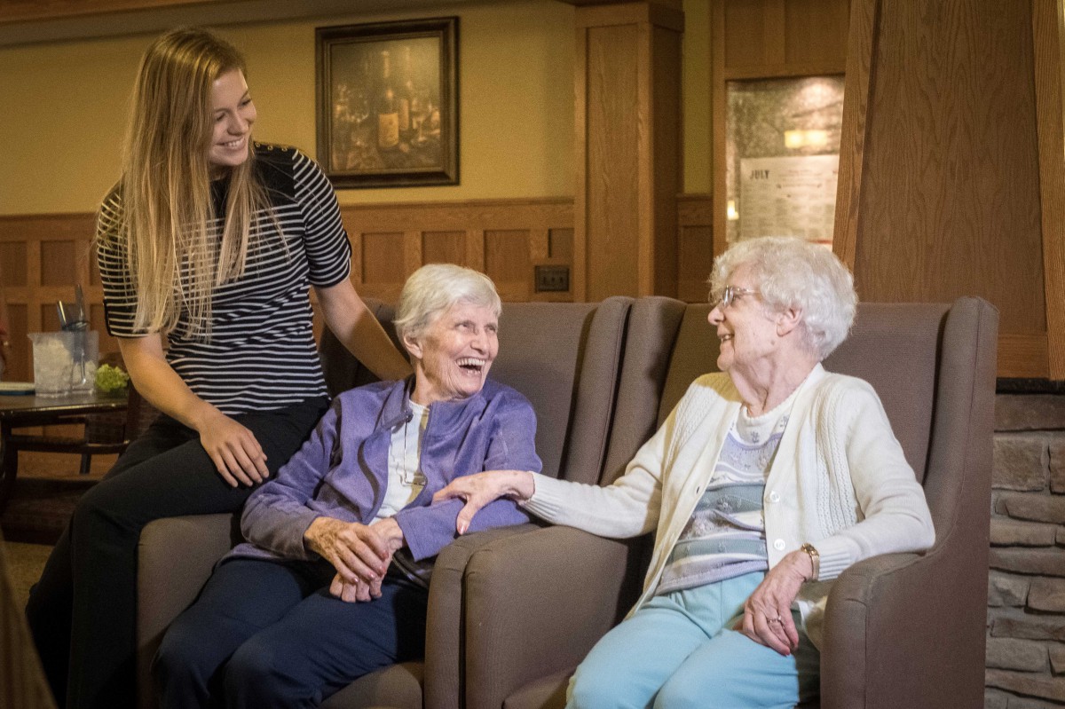 Two elderly women enjoy a lively conversation with a caregiver.