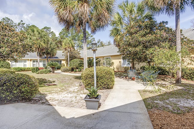 A scenic view of a residential garden with a walkway lined with palm trees.