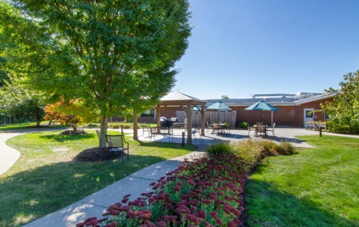 A peaceful outdoor garden with a pathway, trees, and a gazebo on a sunny day.