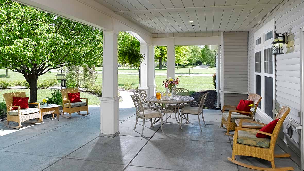 A cozy covered patio with outdoor furniture, overlooking a lush garden.