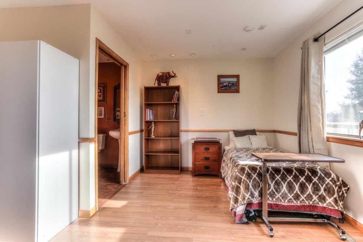 A cozy room featuring a bed, bookshelf, and wooden flooring.
