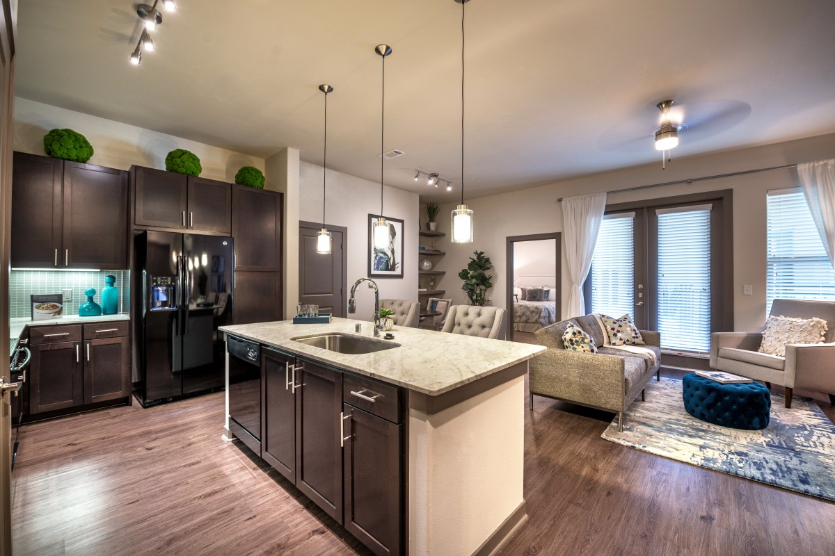 A modern open-concept kitchen and living room featuring hardwood floors, a kitchen island, and pendant lighting.