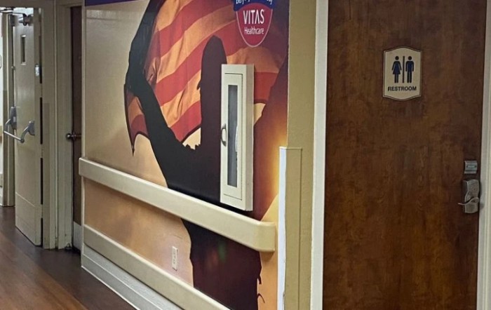 A hallway mural featuring a silhouette of a person holding an American flag, located near a restroom sign.