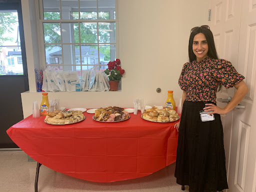 A woman stands beside a table filled with a variety of snacks and refreshments, ready for an event.