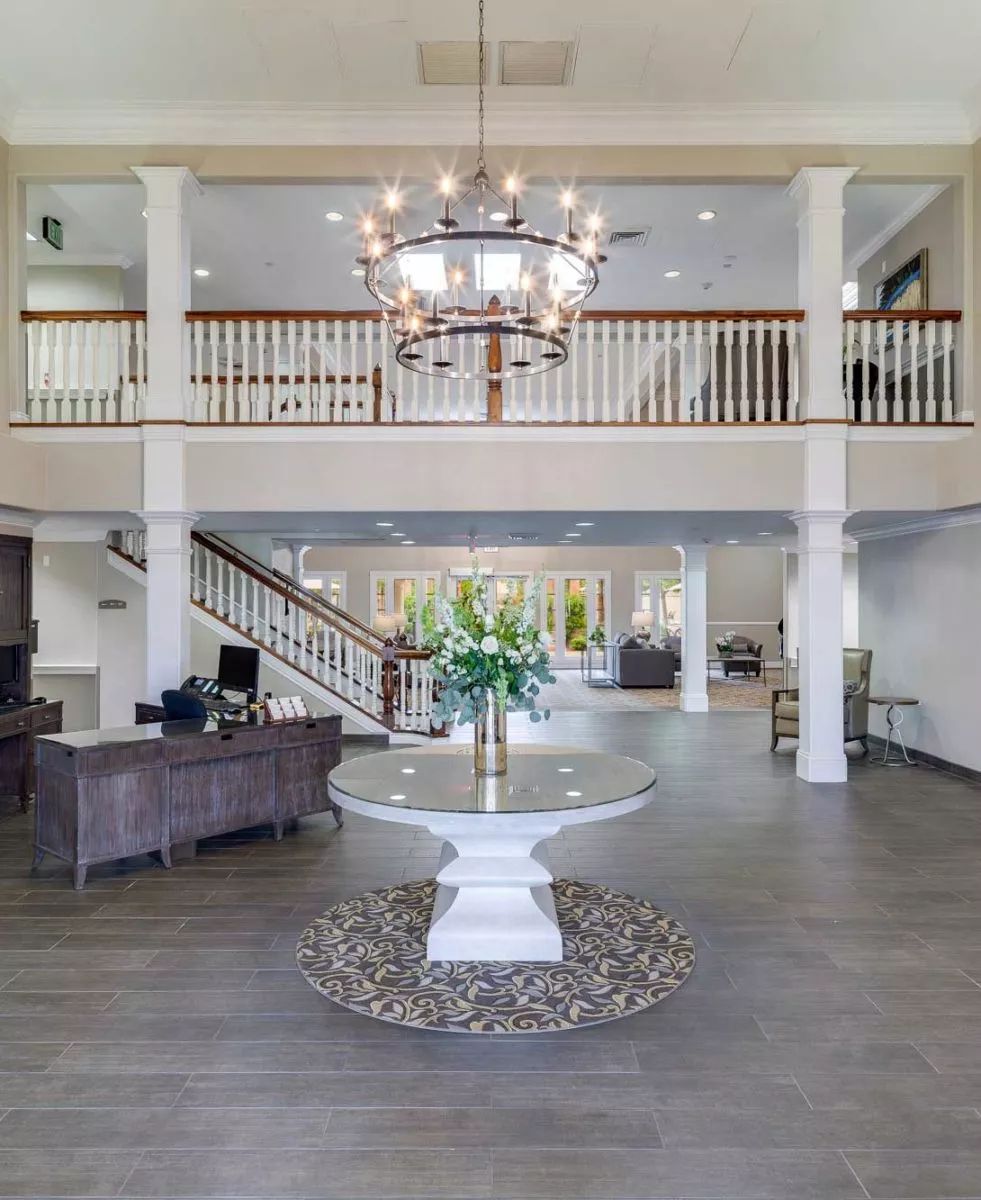 A spacious hotel lobby featuring a grand chandelier, elegant staircase, and stylish reception area.