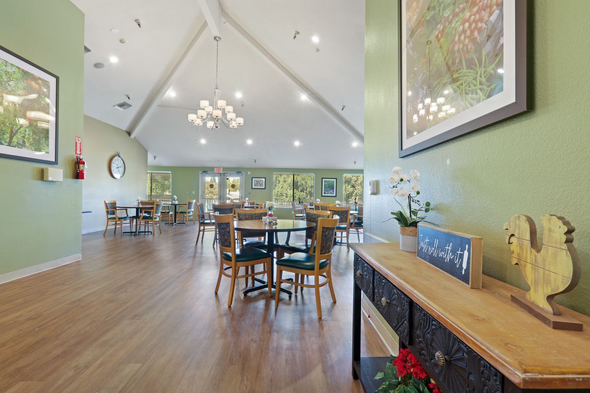 A spacious dining area with elegant chandeliers, green walls, and neatly arranged tables and chairs on a wooden floor.