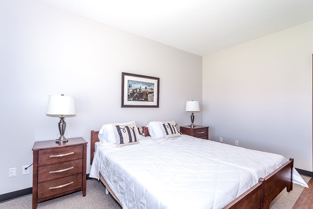 A bright and neatly arranged bedroom featuring a double bed with white bedding, flanked by two wooden nightstands and lamps.