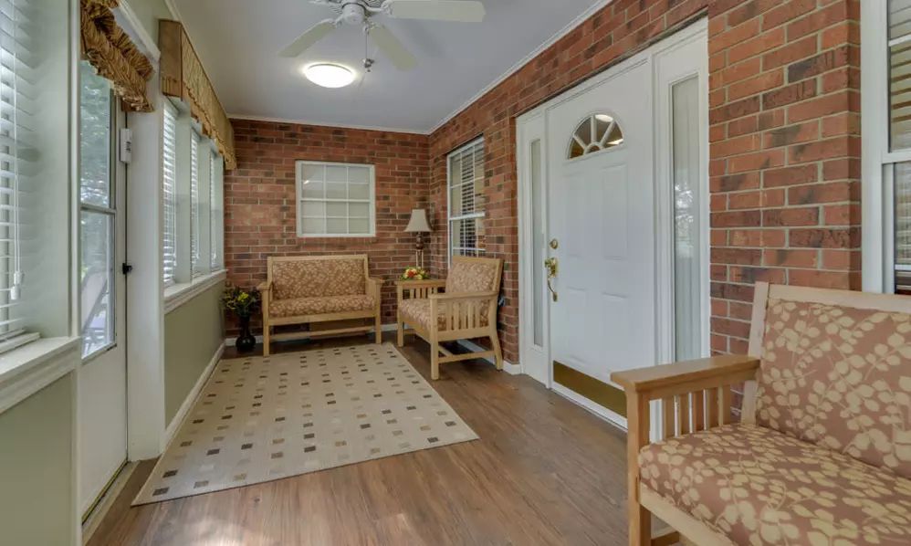 A cozy sunroom featuring brick walls, wooden furniture, and a large window letting in natural light.