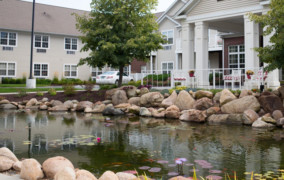 A serene pond with surrounding rocks in front of an apartment building.
