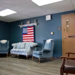 A waiting room featuring a display of the American flag, with blue couches and chairs against a teal wall.