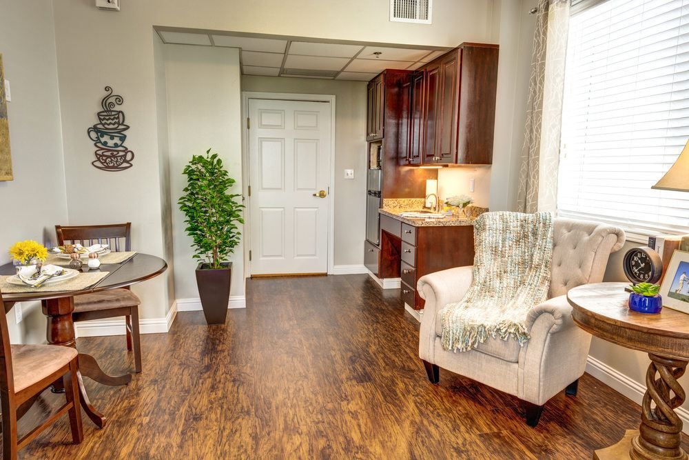 A cozy living space featuring hardwood floors and an armchair, with a kitchenette and potted plant.